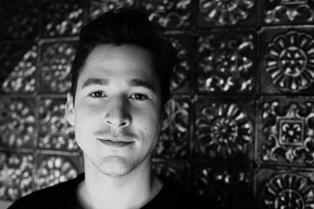 Tommy, private experience curator, black and white portrait against a patterned tiled wall